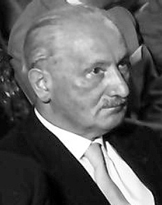 Dtail d'une photographie en noir et blanc dune personne assise, de profil, moustachue, relativement ge, regardant fixement droit devant elle. A l'air dcouter un orateur lors dune confrence.